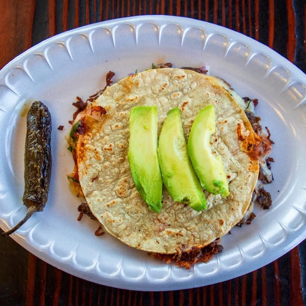A Tacos Chapala quesadilla with avocado slices and a grilled jalapeño on a white plate.