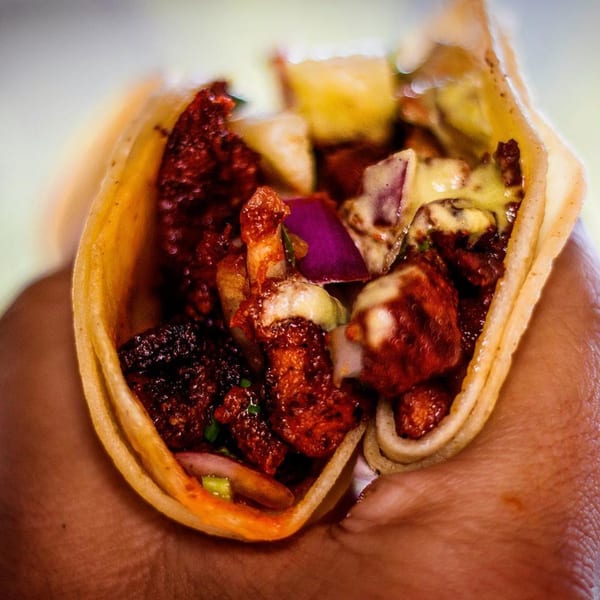 A hand holding a Tacos Chapala taco filled with red meat, purple onions, and white sauce.