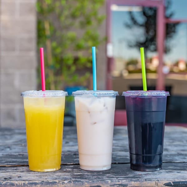 Three colorful Mexican aguas frescas drinks with straws on a rustic wooden table.