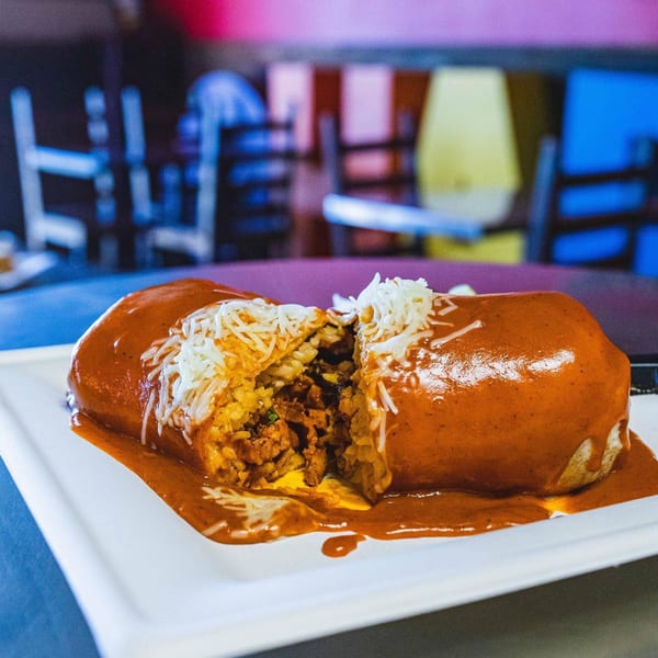 A large, saucy burrito, cut in half, revealing rice and meat filling on a white plate.