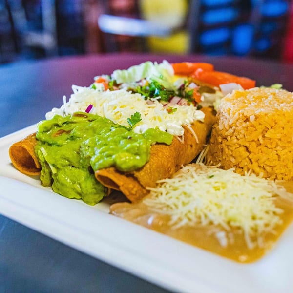 Tacos Chapala's Mexican dish with taquitos, guacamole, rice, beans, and shredded cheese.